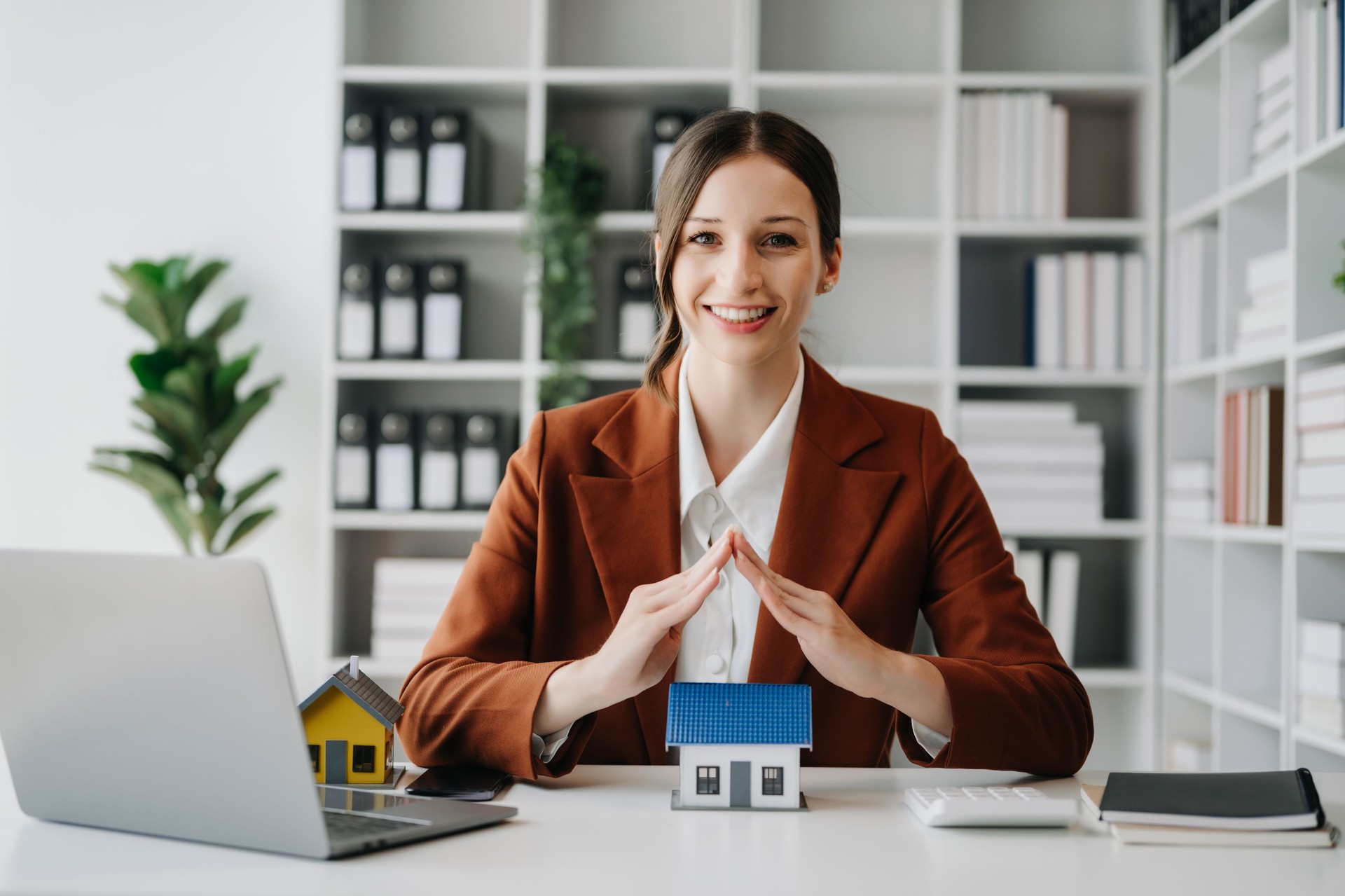 Female real estate agent is use hands to protect red roof for the concept of real estate investment about house trading, purchase at desk in office